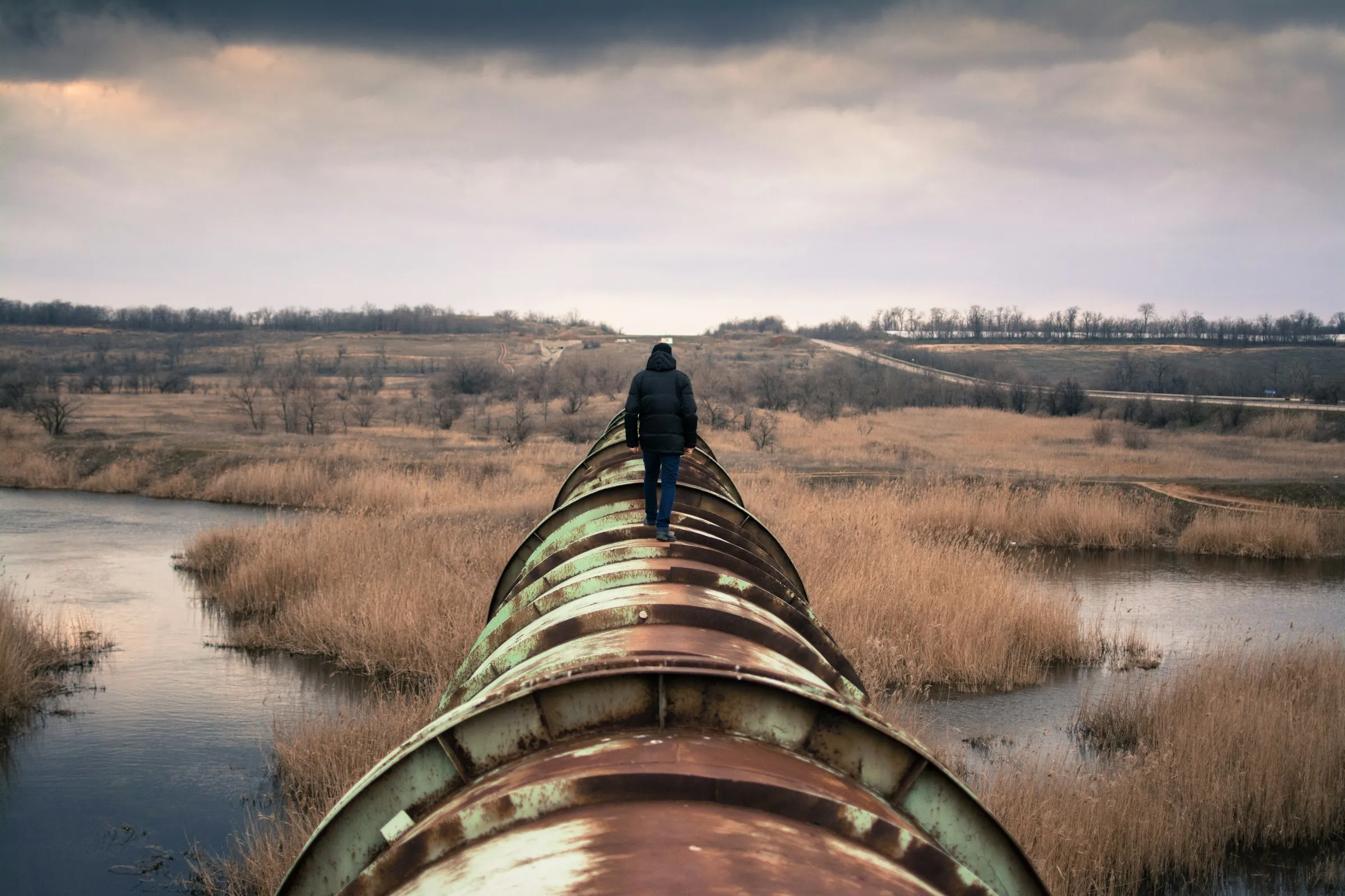 A person balances on a large pipe, with a view of the landscape in the background.