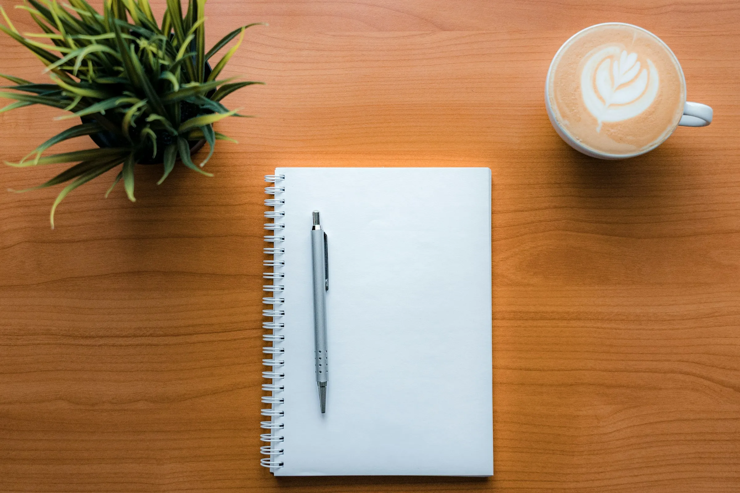 A wooden table displays a notebook, a pen, and a steaming coffee cup, suggesting a productive writing session.